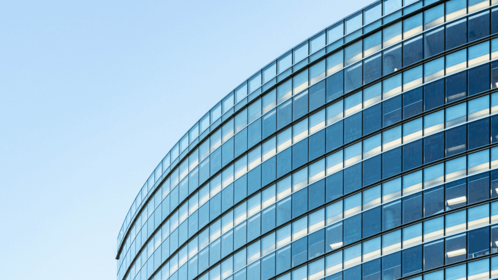 Curved facade of a modern glass office building with multiple floors, reflecting a clear blue sky. The image shows clean architectural lines and numerous windows.