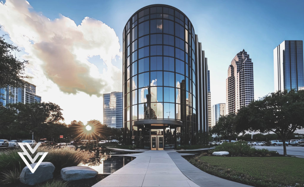A modern glass office building with a rounded front is shown at sunset, reflecting the sky and clouds. The building is surrounded by trees, a sidewalk, cars, and tall city skyscrapers. A white geometric logo is in the corner.