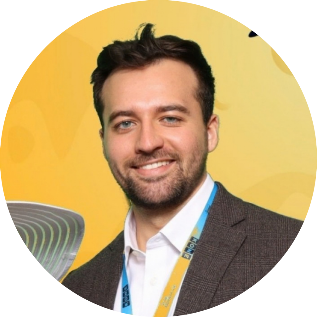 A smiling man in a blazer wearing a conference lanyard.